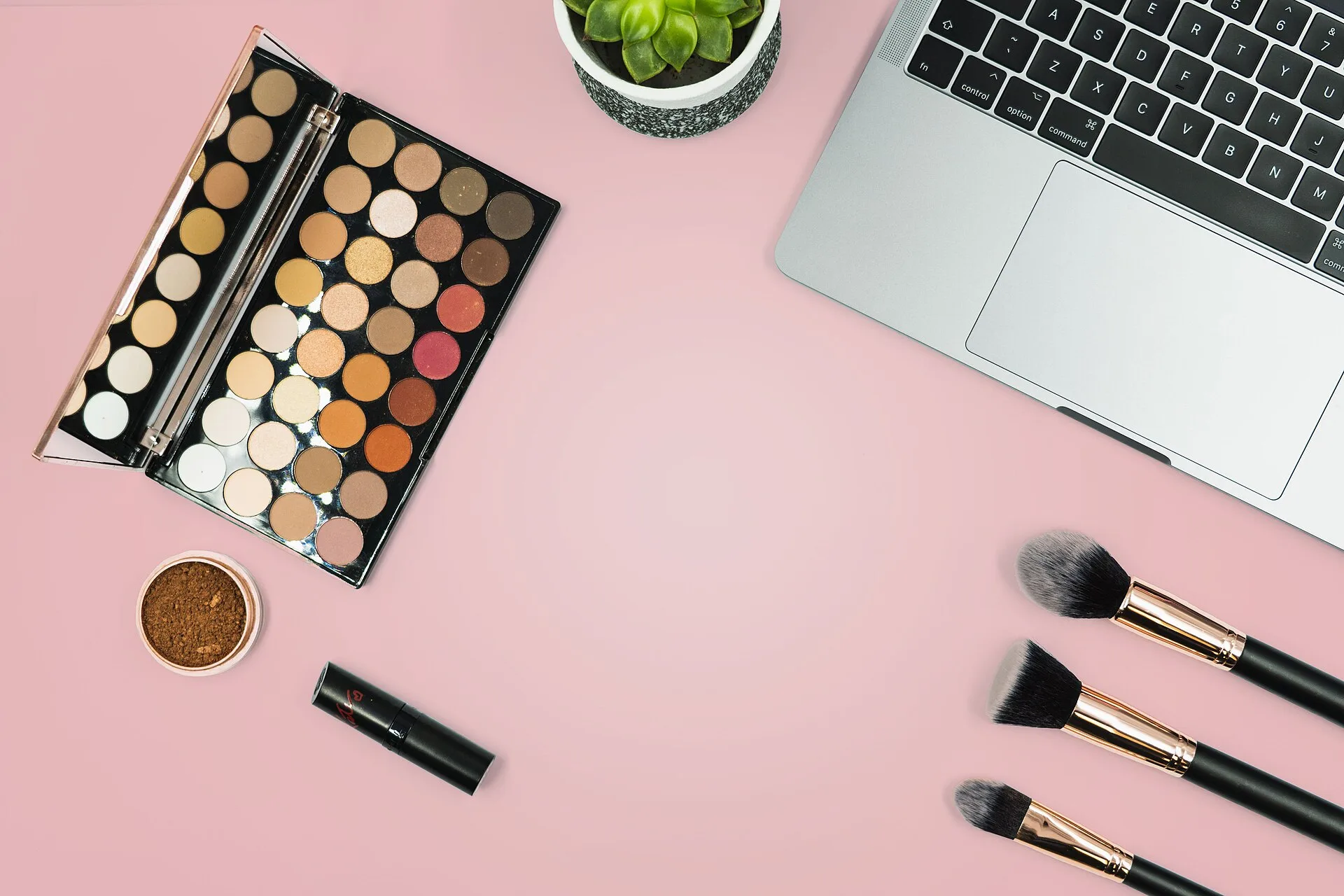This photo shows a range of make up and make up brushes on a pink background next to a laptop as a beauty blogger gets ready to update her make up blog. We took this image during our own shoot, but have now decided we'd like to share it by releasing it under Creative Commons. Please feel free to use